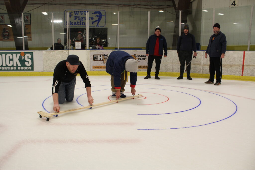 Eric McLaughlin, left, and Ryan Hand draw curling targets on the ice at the Morgantown Ice Arena Saturday night in preparation for the Morgantown Curling Club’s “Learn to Curl” event as other members of the club look on.