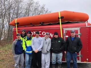 seven man standing in front of a red trailer with an inflatable raft on top